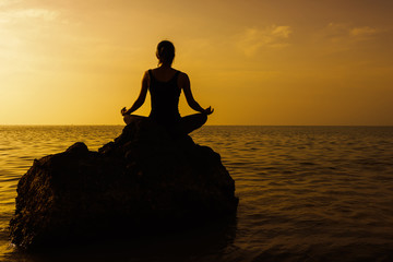 Silhouette of woman practicing yoga on the rock during a beautif