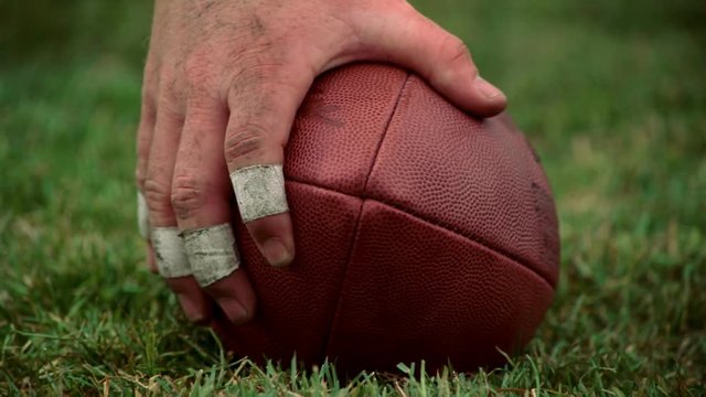 Eye-level close-up of football on turf and hand reaching to tilt it