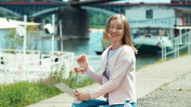 Young adult holding tablet pc outdoors near river. Smiling at camera