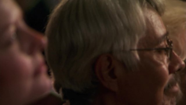 Rack-focus of attentive worshipers' faces in a seated congregation