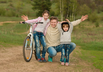 father with two little daughters walking with bike in a countryside