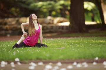 Young woman doing yoga exercises in park's lawn. Girl in pink sport wear sitting in yoga pose in the park.
