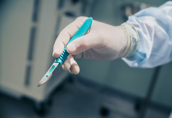 closeup of a scalpel in hand on the background of the operating room