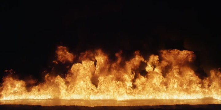 Flames rise across the frame from a pool of liquid fuel