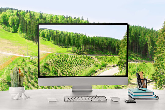 Conceptual image of a work space and computer desktop with tall green trees over blue sky background