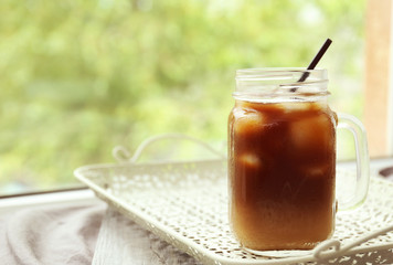 Glass jar of iced coffee on blurred natural background