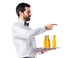 Waiter with beer bottles on the tray pointing to the lateral