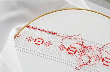 The wooden hoop with the embroidery pattern of red and white color on canvas.