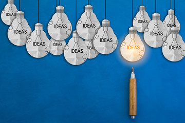 Glowing light bulbs with pencils on blue leather background