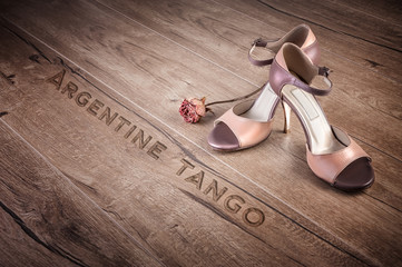 Argentine tango shoes and a dry rose on wood, text