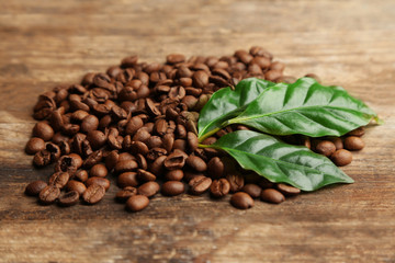 Coffee beans and green leaves on wooden background