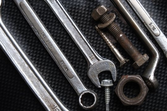 Nut wrenches on a reflective carbon fiber surface with nuts and bolts. Tools and equipment