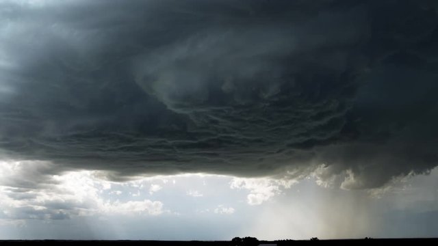 Dark supercell cloud unloading rain or hail over a prairie landscape