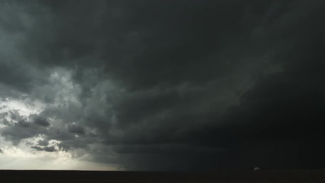 Low fast-moving thunderstorm rolls across prairie as headlights speed by at right, time lapse