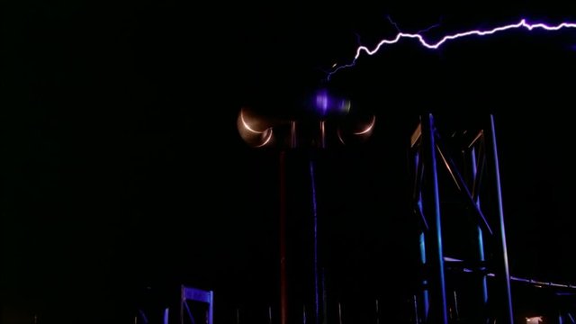 Electric arcs from Tesla coil striking metal trusses as camera dollies right