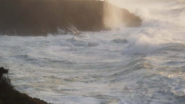 Powerful foaming waves crash into a rocky cove along a storm-battered shore