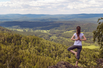Naklejka premium Woman practices balance yoga asana Vrikshasana tree pose in moun