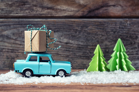 Toy car carrying a Christmas gift with snow and paper fir trees