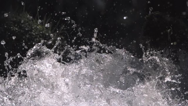 Ultra-slow motion water drops flung up by splashing whitewater in a mossy stream