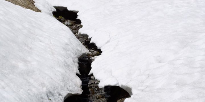 Tilt-down to path of tiny stream bordered by thawing snow