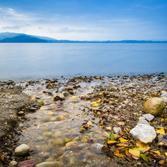 Autumn landscape on the lake. On the shore are colored stones and fallen leaves.