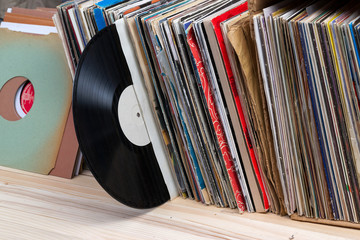 Retro styled image of a collection of old vinyl record lp's with sleeves on a wooden background. ...