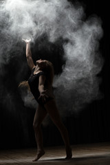 Ballerina dancing with flour on black background