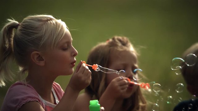 Faces of two little girls blowing ultra-slow motion soap bubbles