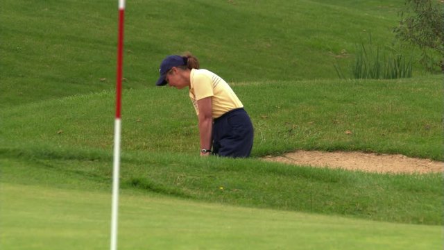 Woman golfer popping ball up out of a sand trap and onto green