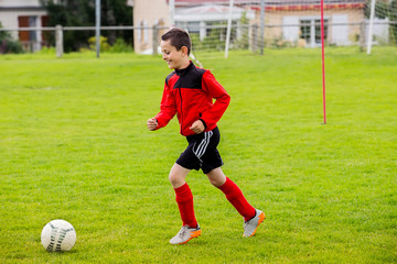 Obraz premium Little Boy playing soccer on the sports field.Training little boy on a asport field.Boy running with a soccer ball on a country sport field .