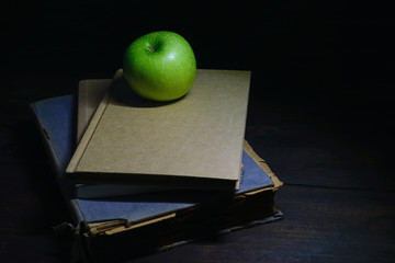 Green apple with old book on black wood background, dark tone.