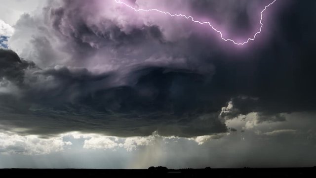 Swirling dark gray supercell cloud with lightning and rain over a prairie landscape, time lapse