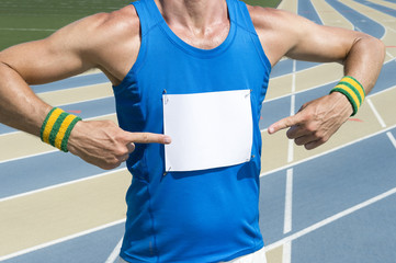 Brazilian athlete in Brazil pointing with colored wristbands at blank race bib standing in front of the running track