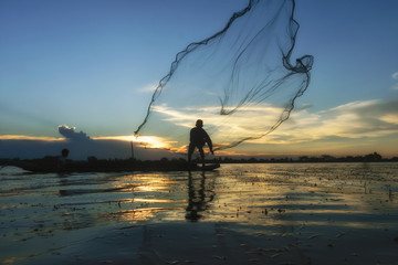 Traditional Asian fishermen throwing net fishing in the river at sunset time.