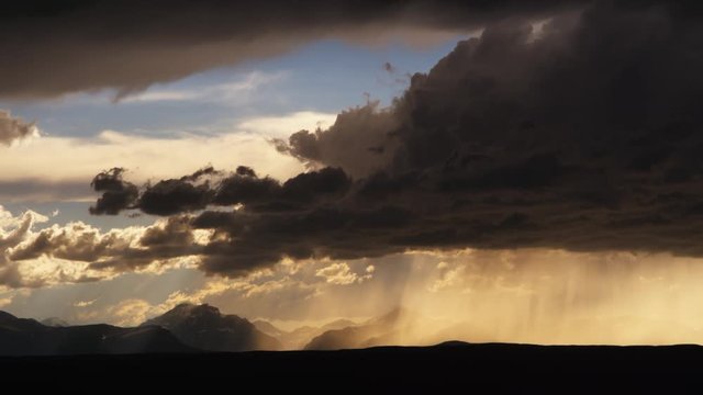 Hurrying dark upslope supercell spilling rain in foreground with lighter clouds and blue sky over mountains, in rear, time lapse