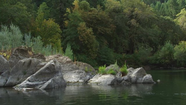 Floating past boulders at river's edge to reveal wooded shoreline