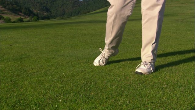 Close view of club head hitting golf ball out of frame, golfer's legs shown