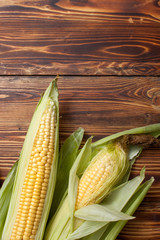raw cobs of young corn with leaves on a wooden table