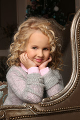 Cute little blond girl sitting peering over chair arms