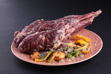 Fresh and raw meat. Uncooked Leg lamb with salt, peel of citrus fruits on black background. 