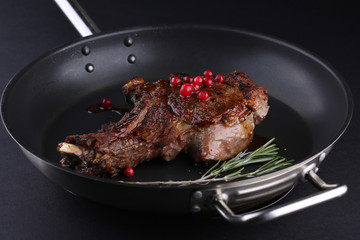 Rustic roast lamb with juices and rosemary on pan, dark background.
