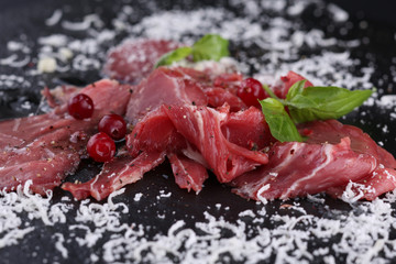Beef carpaccio with parmesan cheese and greens on the black background