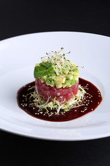Smoked salmon, avocado, arugula, mikrogrin and the sauce with cumin on white plate, dark background