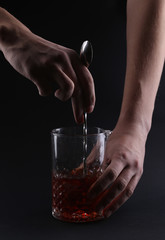 Cocktail in a glass, mans hand, spoon on dark background