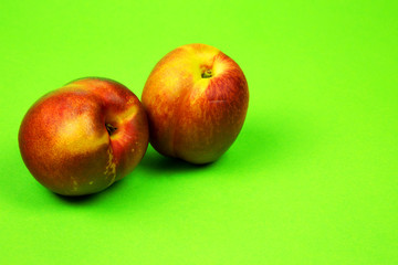 Two fresh nectarines on a bright green background