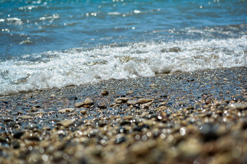 Мелкие камни на берегу моря и морская волна.