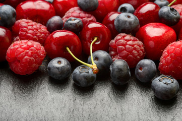 Summer berries (blueberries, raspberries and cherries) on black background. May be used for text.