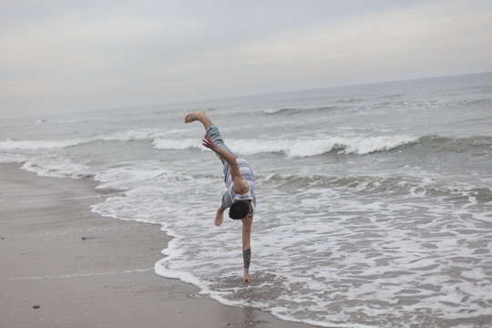 A young man doing a handstand on the beach