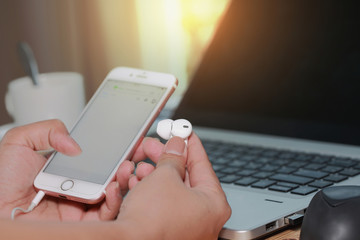 Selective focus of Hands holding hand holding earphone and blank screen of white smartphone device  on computer keyboard as technology and telecommunication concept.