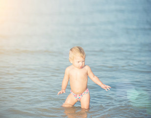 Fototapeta na wymiar Baby playing on the sandy beach and in sea water. Cute little kid with toys on sand tropical beach. Ocean coast.